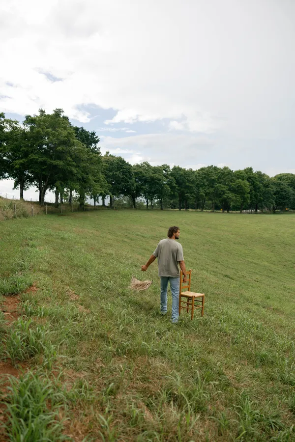 A man carrying a chair and basket across a field at dusk